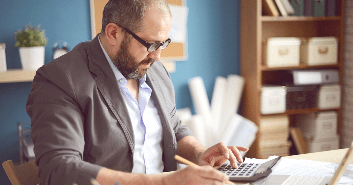 A man sitting at a desk, using a calculator to do some accounting work.